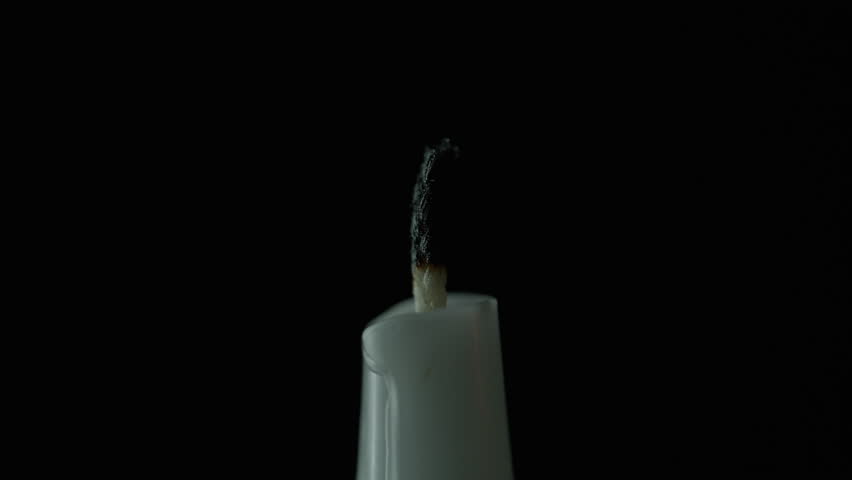 Extinguished candle black background closeup. Hand holding wooden match sparking paraffin taper on dark isolated wall. Flame shining strongly with warm fire glowing inside dim room. Memory concept