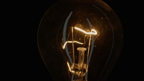 Incandescent bulb turns on and off flickers on black background closeup. Warm flashing filament on isolated. Glass old lightbulb glowing yellow light. Heated wire inside shines with golden pulses - Powered by Shutterstock - Get 15% off with code: PIKWIZARD15