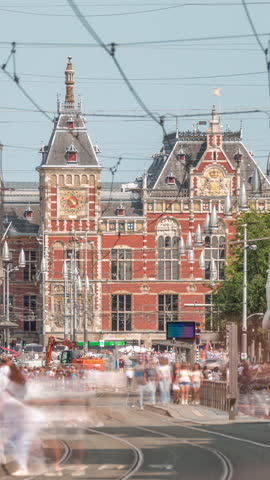 Damrak Street heading from Dam Square to Centraal Station in a timelapse with electric tram. Traffic moves on the road while people wait at the tram stop. Amsterdam, Netherlands
