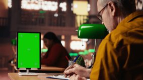 Aged old man using isolated mockup screen on tablet at a public library, reading educational papers and committed to completing his studies. Quiet study room senior education. Camera B. - Powered by Shutterstock - Get 15% off with code: PIKWIZARD15