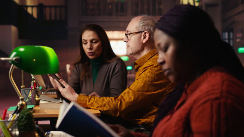 Colleagues disturbing a woman with their loud reading in the library, african american pupil making a noise complaint and being disturbed by the disrespect. Breaking the rules. Camera B.