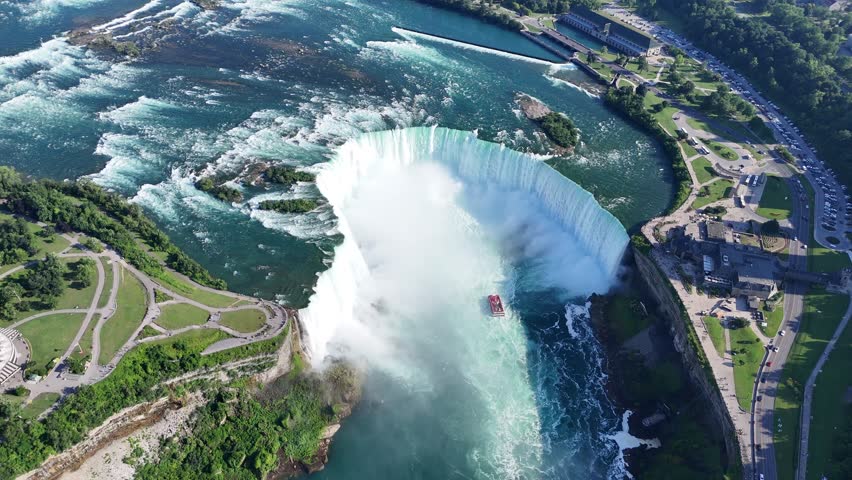 Drone flies sideways from Niagara Falls State Park, circling Horseshoe Falls toward the Trans Canada Trail observation point on the Canadian side, as Maid of the Mist cruise ships head into the mist