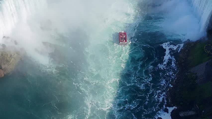 Drone captures a top-down close-up of Maid of the Mist cruise ships in the Niagara River, then flies toward the falls revealing turbulent base currents and continues to the cliff edge with cascading w