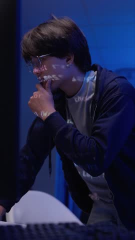 Focused Asian young adult male programmer analyzes complex code. Digital projections highlight innovative technology solutions.