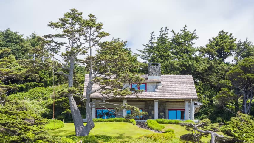 A beautiful home sits on Cannon Beach, Oregon, overlooking the Pacific Ocean with green forest behind and waves rolling onto the sandy shore in this 4K video.