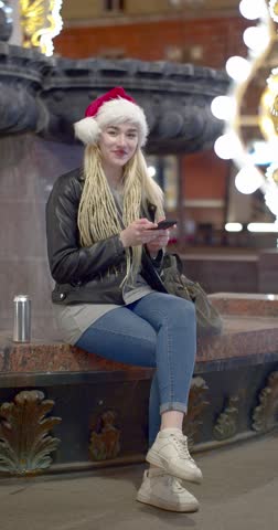 Young Caucasian woman in santa hat received messages from a loved one on a christmas eve. She is happy. Slow motion 4k footage.