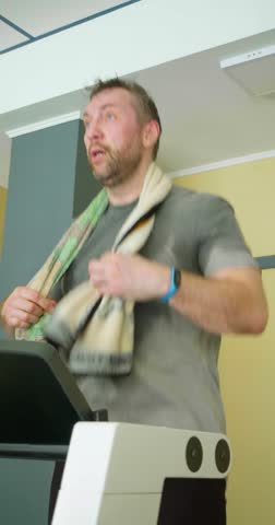 Middle-aged man with a towel on his neck during heavy treadmill workout. Slow motion vertical 4k footage.