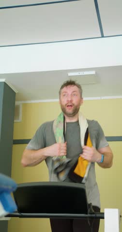 Heavy treadmill workout. Keeping fit in your 40s - middle-aged man with a towel on his neck running on a treadmill. Slow motion vertical 4k footage.