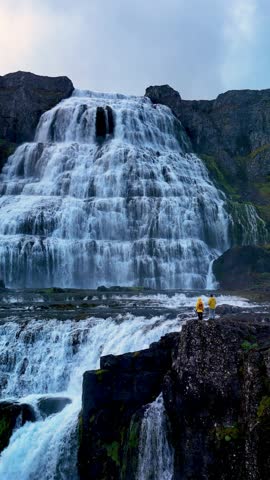 Dynamic water flows from the high cliffs of Dynjandi waterfall, creating a stunning display in the scenic Icelandic wilderness. Visitors marvel at the natural beauty under dramatic skies.