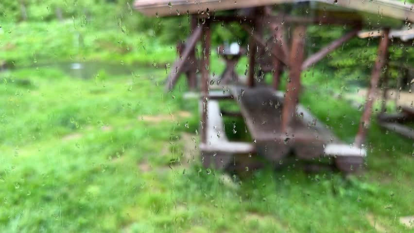 Blurred view of the wooden gazebo through a wet window covered with water drops during a rain
