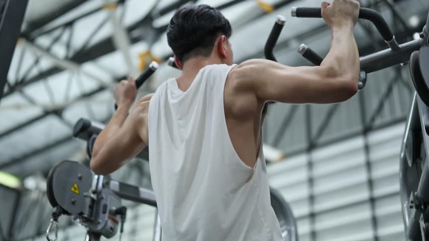 Muscular sportsman performing challenging pull up exercise, demonstrating strength, fitness, and physical dedication while training back muscles at modern gym facility