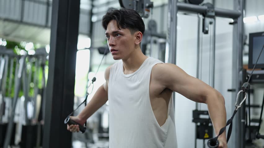 Muscular sportsman performing cable crossover exercise, targeting pectoral muscles with intense focus and controlled movement in fitness center environment