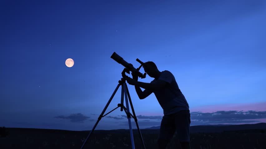 Amateur astronomer using telescope for watching stars, Moon, planets and other celestial objects from a field in nature.