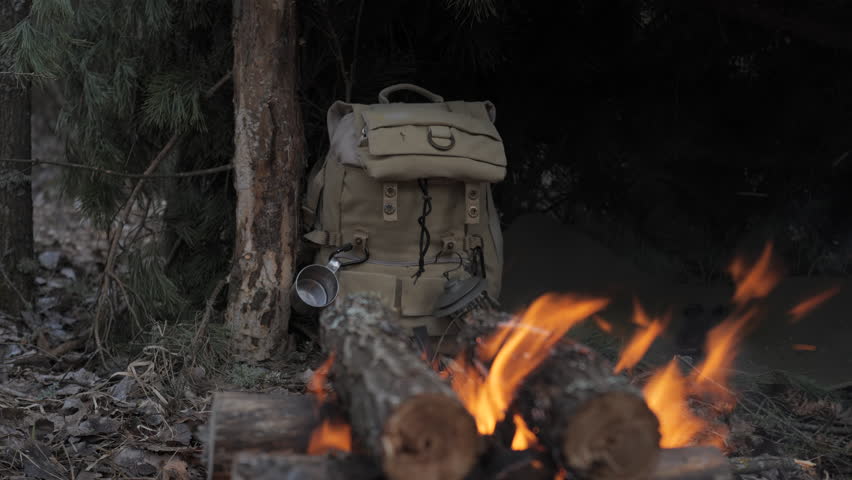 A man prepares firewood in a shelter for survival in the forest, a wildlife survivalist arranges logs near a makeshift shelter using gloves in the cold forest