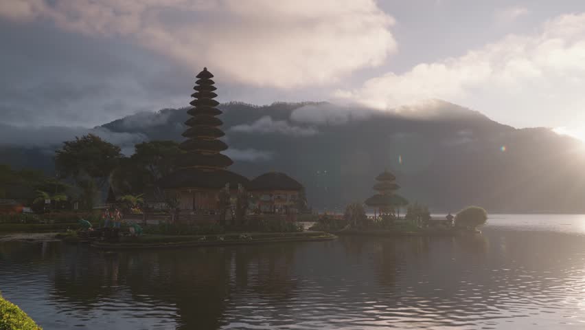 Slow motion sunrise at Ulun Danu Beratan Temple in Bali, Indonesia. Peaceful morning light, misty mountains, and spiritual atmosphere at this iconic lakeside temple.