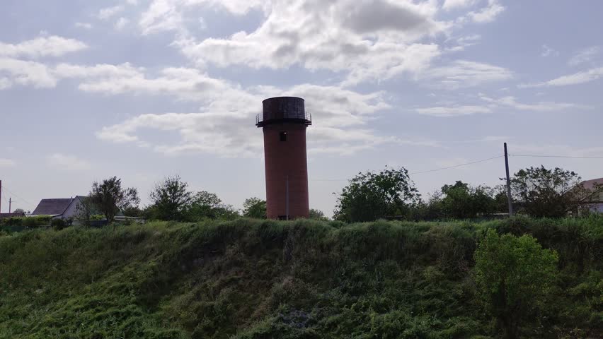 Old leaning brick water tower on a hill against the sky