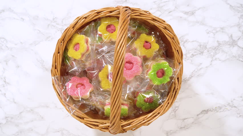 Hands pull a single flower-shaped sugar cookie from a wrapped basket, highlighting its detail. Great for product close-ups, bakery showcases, or dessert promotional content.