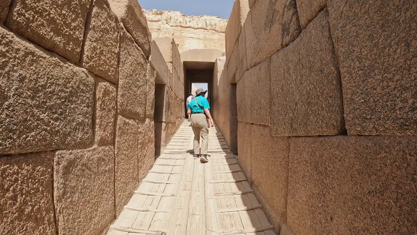 Tourist walks in narrow stone causeway at Giza pyramid complex, Egypt