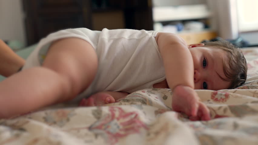 Baby attempting to roll on bed, early motor skills development, playful effort, joyful expression, childhood curiosity, sensory exploration, home environment, growth, determination