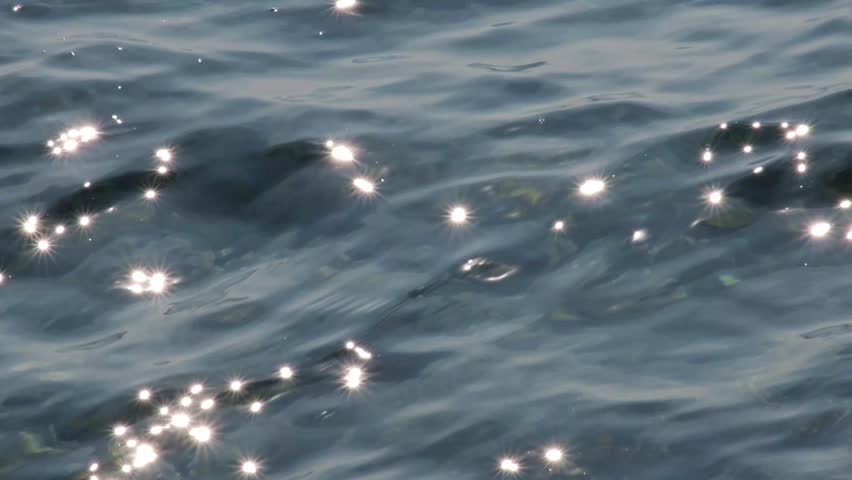 Beautiful sparkling sunset reflections on dark blue water surface. Continuously changing wavy sea surface for background. Neutral mirror effect, sun glittering around. Summer, enjoying water.