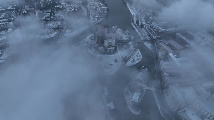 Foggy aerial view of snowy Wroclaw and Oder River with Cathedral Island emerging through thick mist at sunrise in Poland