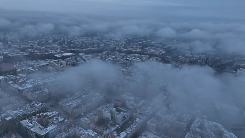 An aerial view of Wroclaw, Poland covered in snow and fog, with clouds partially hiding buildings and streets during daytime