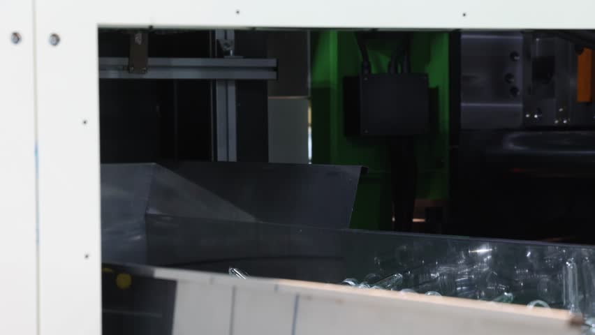 PET bottle preforms line. Plastic bottle preforms on conveyor belt in automated manufacturing system. Industrial injection molding and high speed production in a modern plastic packaging PET factory.