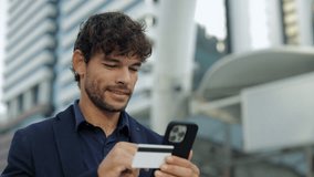 Portrait of smiling Hispanic man pays online with smartphone and credit card near office building. Latin businessman uses digital banking on cellphone and stands in downtown block - Powered by Shutterstock - Get 15% off with code: PIKWIZARD15