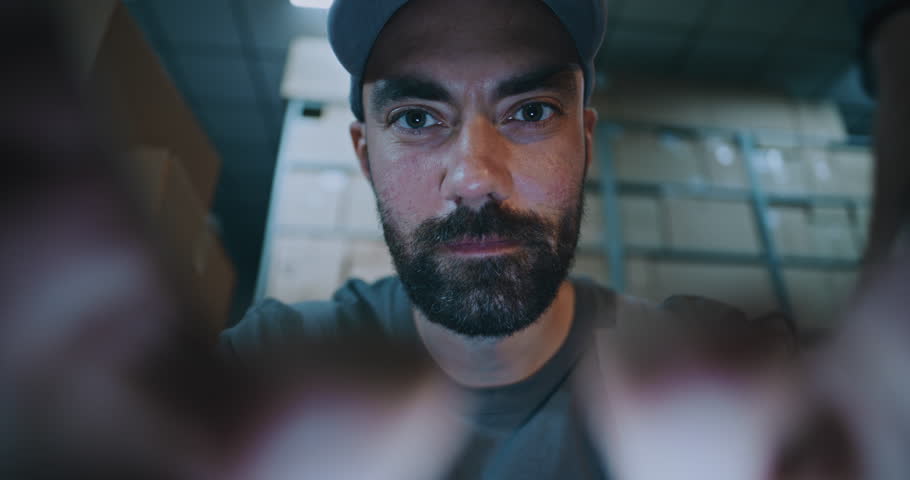 POV from Smartphone Screen: Male Worker Using Phone, Chatting in Social Networks. In the Background, Diverse Employees Carrying Cardboard Boxes with Online Orders in Logistics Warehouse at Night.