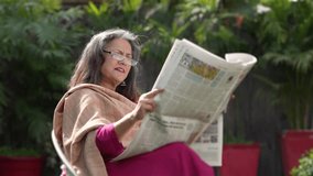 Relaxed senior woman sitting on chair at out of home reading newspaper. - Powered by Shutterstock - Get 15% off with code: PIKWIZARD15