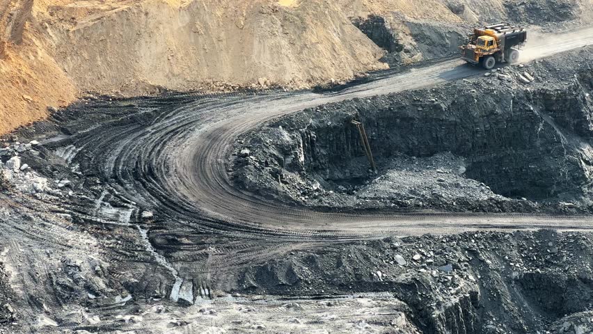 wide shot of a open coal mine in india, A big water sprayer tanker dump truck moving into an open pit coal mine