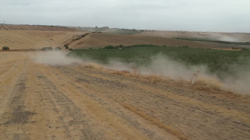 Dust and sand blow across dry agricultural fields and olive groves during strong winds, arid landscape in Andalusia, Spain. Aerial drone, low flight