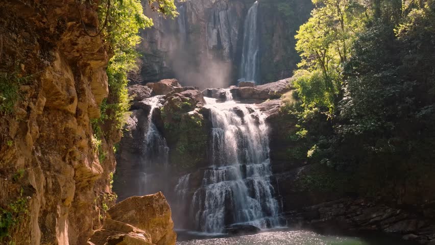 A spectacular aerial view captures the majestic multi-tiered Nauyaca Waterfall bathed in the soft, golden light of sunrise, nestled within Costa Rica's pristine tropical rainforest.