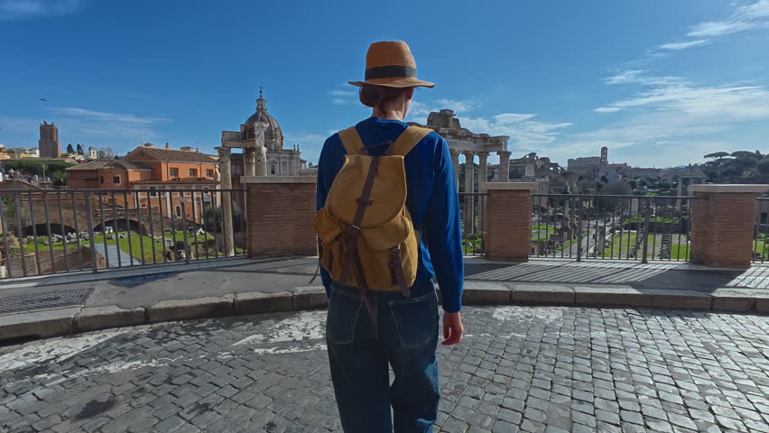 Tourist woman in a hat and with a backpack is considering the sights Columns of ancient Rome at the Roman Forum. Italy. View of a walking girl from the back against the backdrop of landmarks
