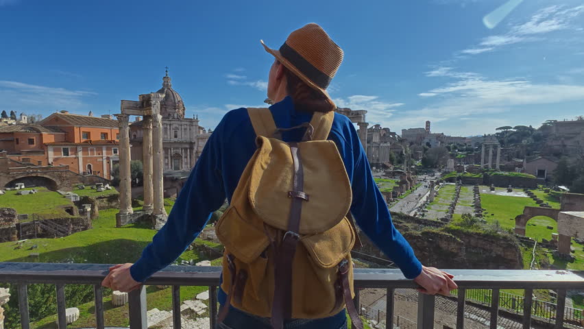Tourist woman in a hat and with a backpack is considering the sights Columns of ancient Rome at the Roman Forum. Italy. View of a walking girl from the back against the backdrop of landmarks