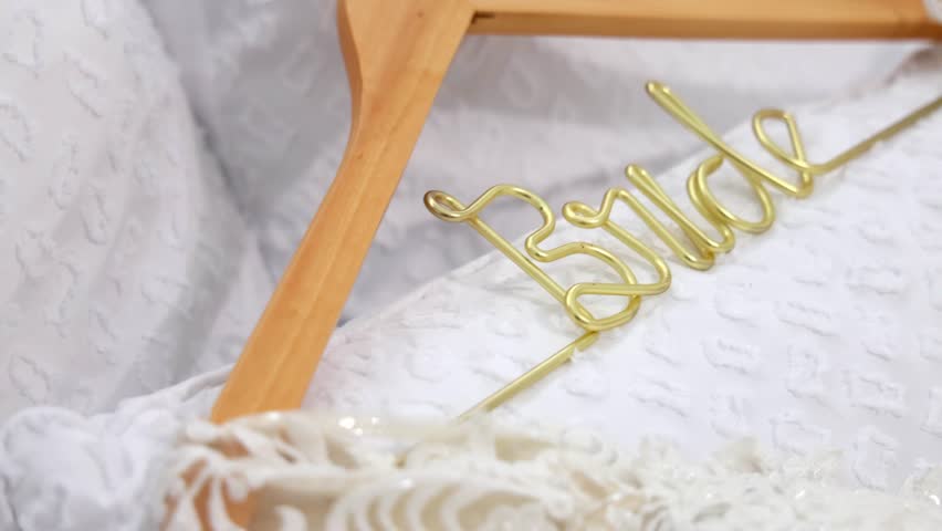 A close-up shot of a wooden hanger with golden "Bride" text, resting on a delicate white wedding dress fabric
