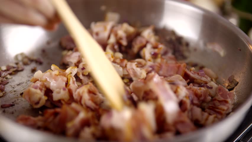 chopped bacon frying in a stainless steel pan, with visible sizzling fat and slight caramelization. Cooking process of savory meat in a kitchen. Smoked strips of bacon. Sizzling meat in pan