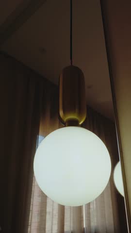 A modern light fixture with a spherical, frosted glass shade and a gold and wood base hangs from the ceiling, reflected in a nearby mirror. interior design, home decor,