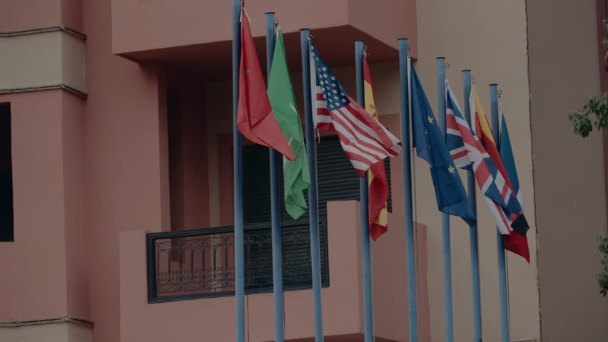 Flags of different countries waving on flagpoles. The flags include the USA, UK, Germany, EU, Morocco, and others. This video symbolizes international relations, cooperation, and global community.