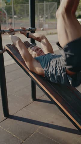 A determined athlete exercises on an incline bench outdoors, focusing on strength and fitness during a sunny day. The image captures dedication and physical commitment. Focused Athlete Exercising