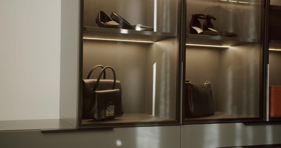 Elegant walk-in closet with shelves, illuminated glass doors showcasing stylish shoes, handbags and storage boxes. Modern design, luxury wardrobe organization, fashion and interior.
