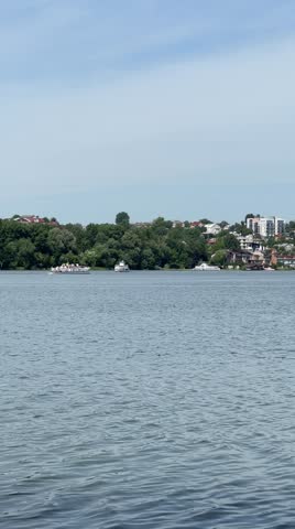 A wide, expansive view across Ternopil Pond (Ternopil Lake) on a bright day, featuring a passenger boat and other vessels on the calm water. The distant shore is lined with lush green trees 