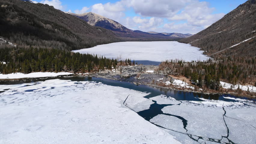 Melting ice on mountain lake reveals rocky riverbed. Media