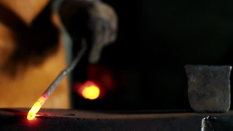 Close up slide shot of blacksmith who shapes hot steal with a hammer