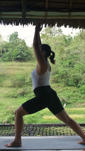 Vertical video. Morning yoga on bamboo hut terrace with tropical view as woman practices balance and mindfulness 
