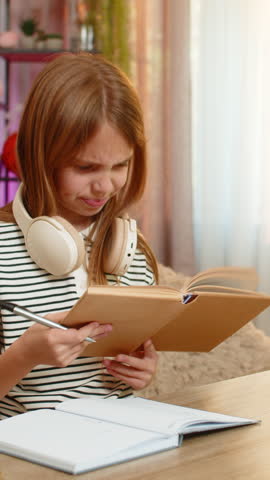 Young child girl sits at home table looks sadly into school textbook struggling to understand the task. School kid holds head in confusion showing frustration and difficulty during homework problem