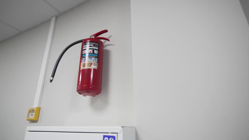 Red extinguisher and alarm button on white wall of office. Fire fighting and warning equipment installed in illuminated building hall