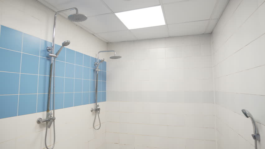 Shiny chrome heads and pipes in tiled public shower cabin. Body washing place with modern equipment in sports club. Personal hygiene