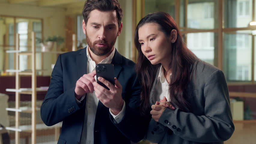 Shocked stressed Caucasian Korean workers afraid use mobile phone losing deal bad news at office shock upset business man woman frustrated entrepreneur businessman businesswoman smartphone sms message