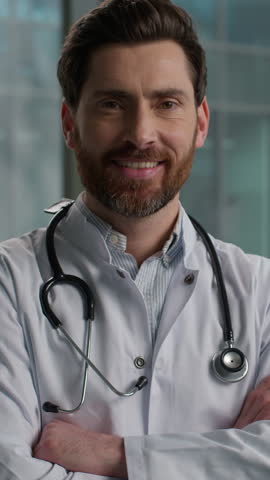 Proud confident Caucasian bearded man male therapist doctor physician doc in lab coat posing looking at camera posing with folded arms consultation medical examination inside clinic hospital hallway